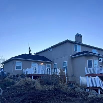 Two-story beige house with white railings and a clear blue sky background.