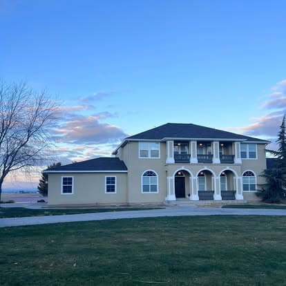 Elegant two-story home with arched entryways, green lawn, and scenic sky backdrop.