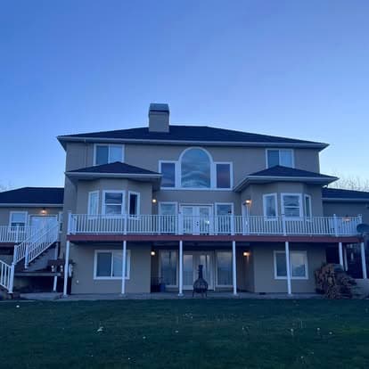 Large two-story house with a balcony and large windows against a twilight sky.