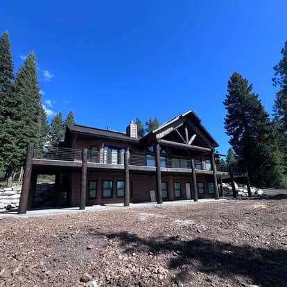 Modern mountain home with wooden accents and large windows, surrounded by trees.